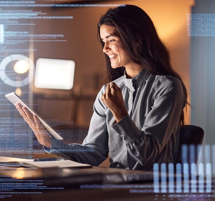 A woman with long dark hair sits at a desk, looking at a tablet and smiling. She has a clenched fist in a gesture of success. The ambient lighting creates a warm atmosphere, and there are digital graphics and data overlays around her.