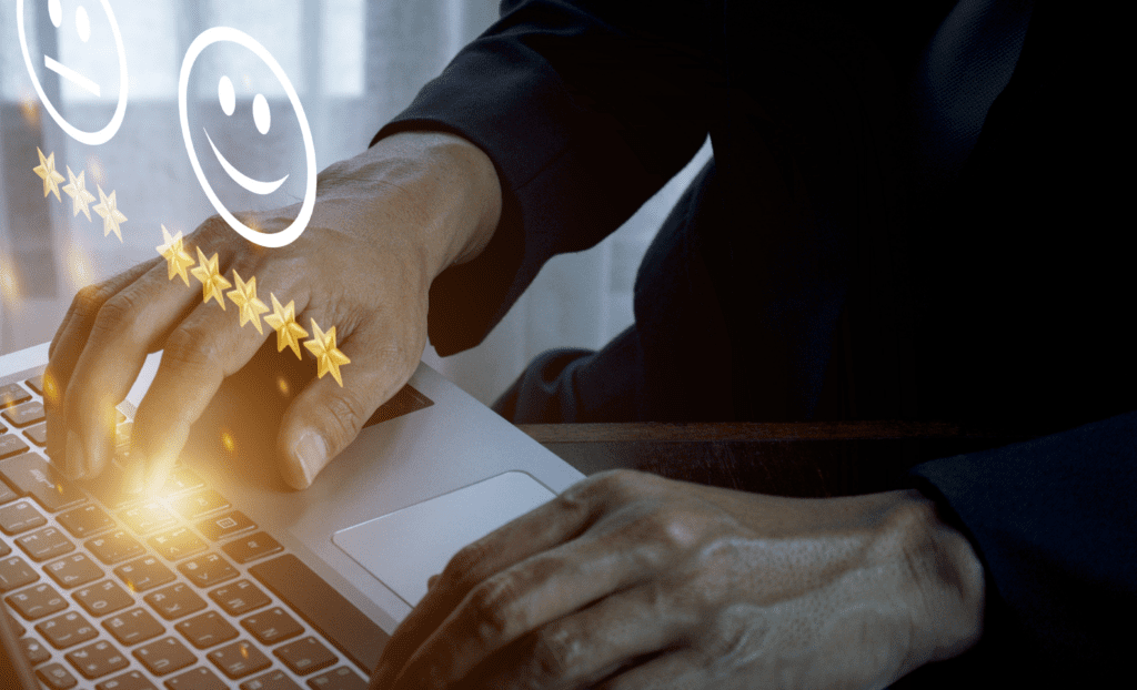 A person wearing a dark suit is typing on a laptop keyboard. Above the laptop, there are two smiley faces and a line of five golden stars, symbolizing positive feedback or customer satisfaction. A curtain is visible in the background.